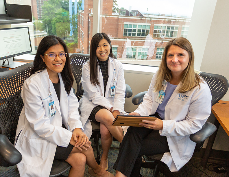 Three female pharmacists are in a group in an office smiling at the camera